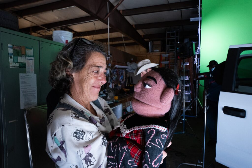 Woman smiling at a puppet in a workshop with green screen, engaged in creative activity.