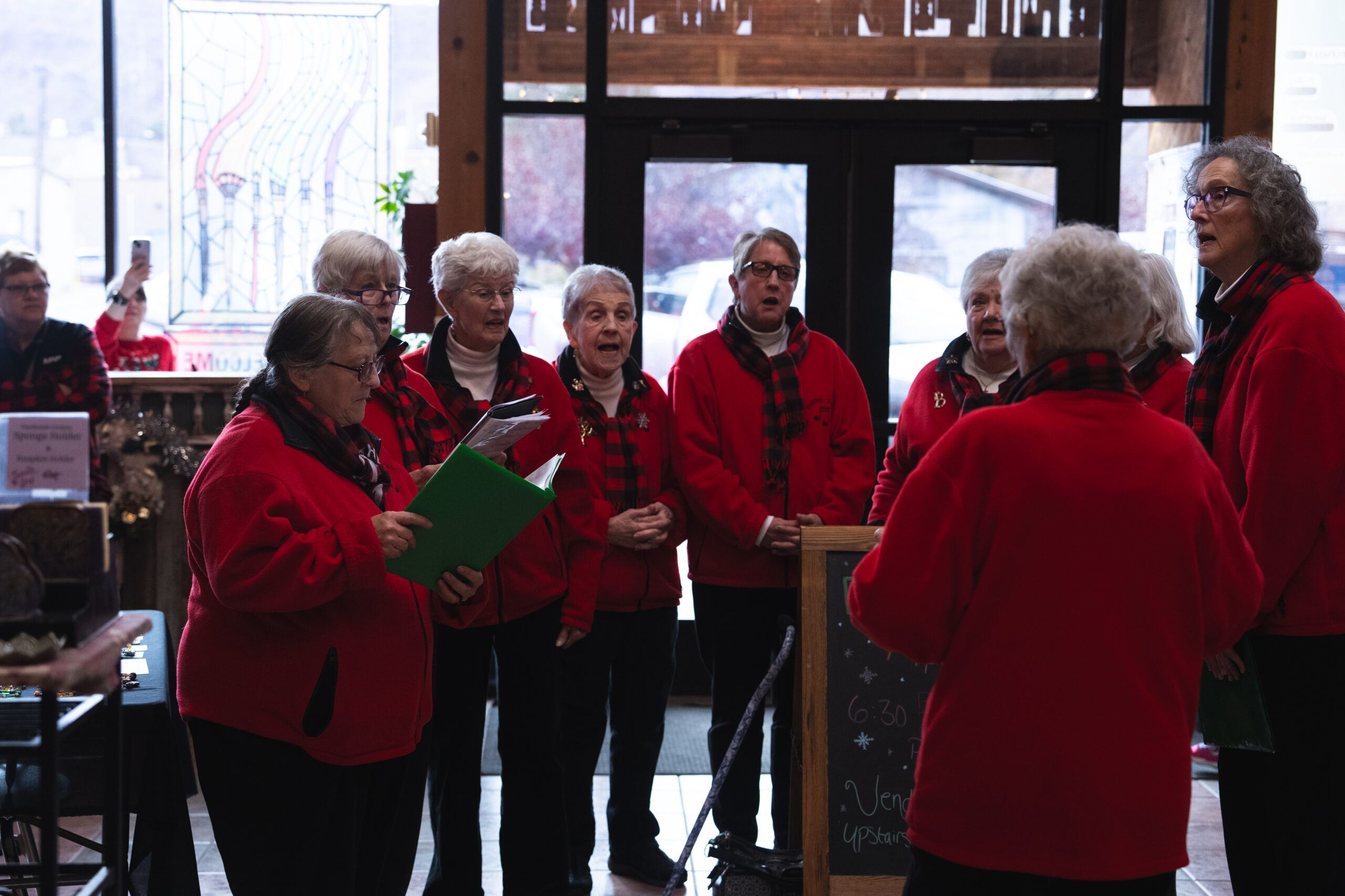Moab Valley Voices singers singing in festive red outfits indoors during holiday market.