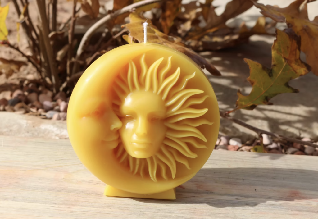 Yellow sun and moon candle sculpture with faces, placed outdoors with autumn leaves in the background.