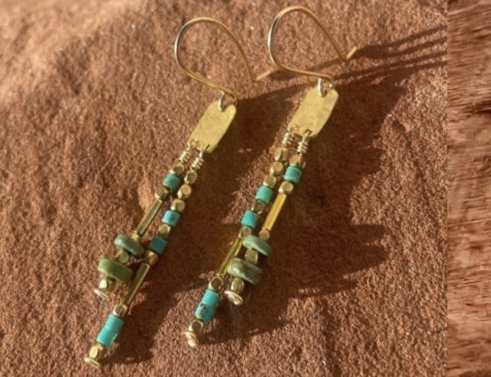 Gold and turquoise beaded earrings on a brown surface, showcasing intricate design and craftsmanship.