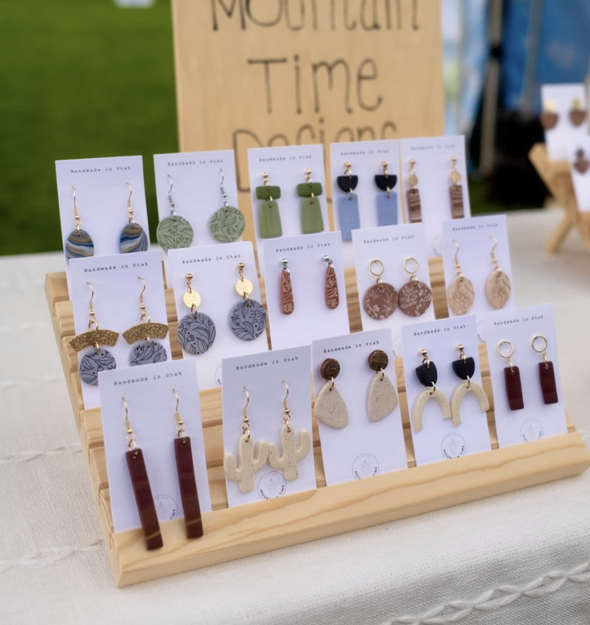 Handmade earrings display with various designs by Mountain Time Designs at outdoor market.