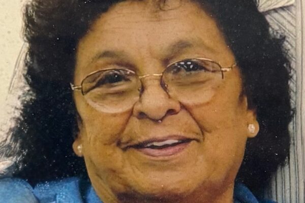 Smiling woman with glasses and curly hair wearing a denim shirt.