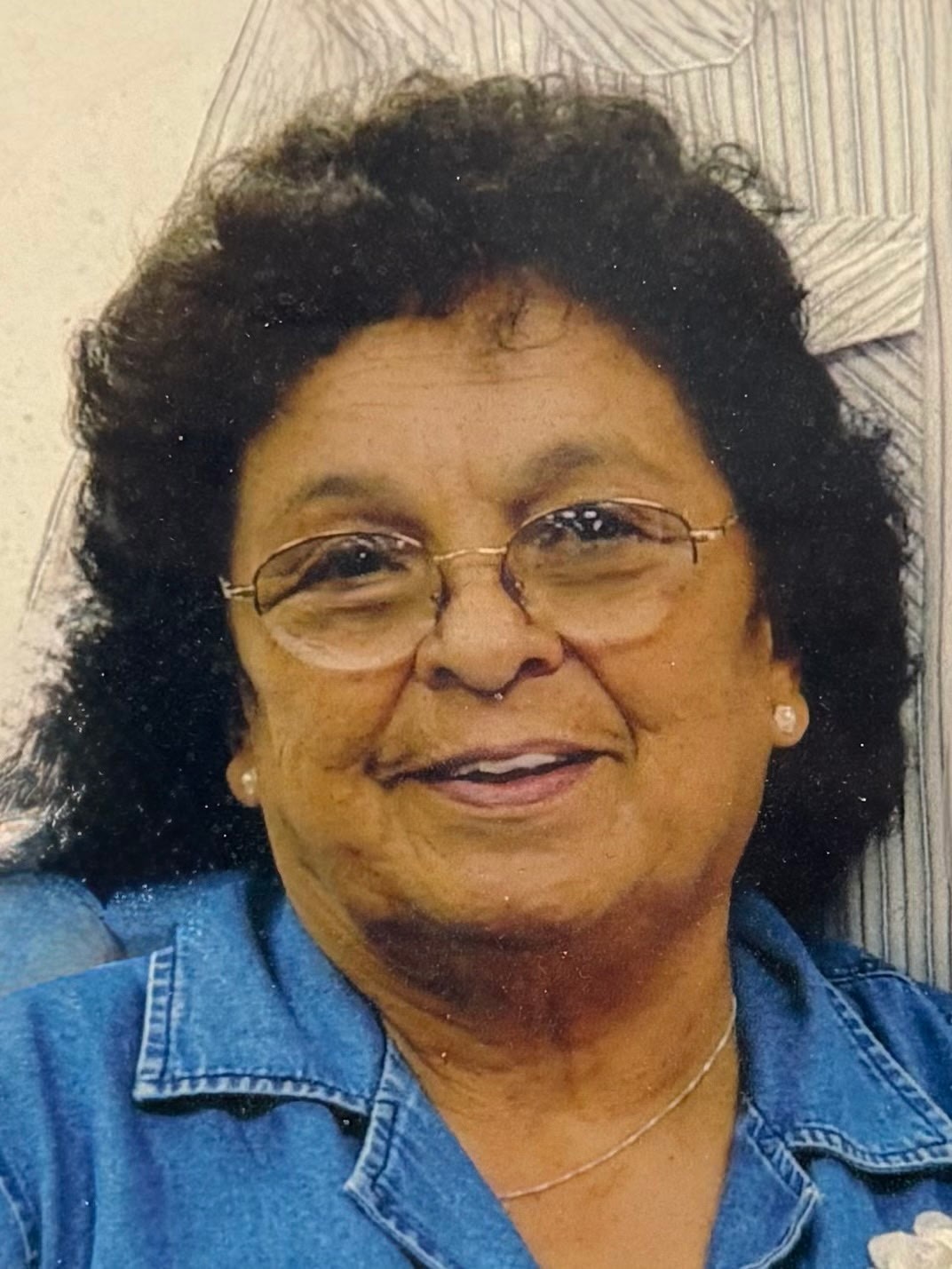 Smiling woman with glasses and curly hair wearing a denim shirt.
