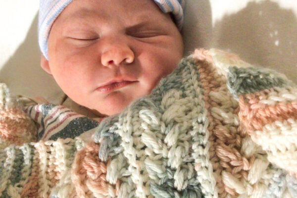 Newborn baby sleeping peacefully wrapped in a cozy knitted blanket with a striped hat.