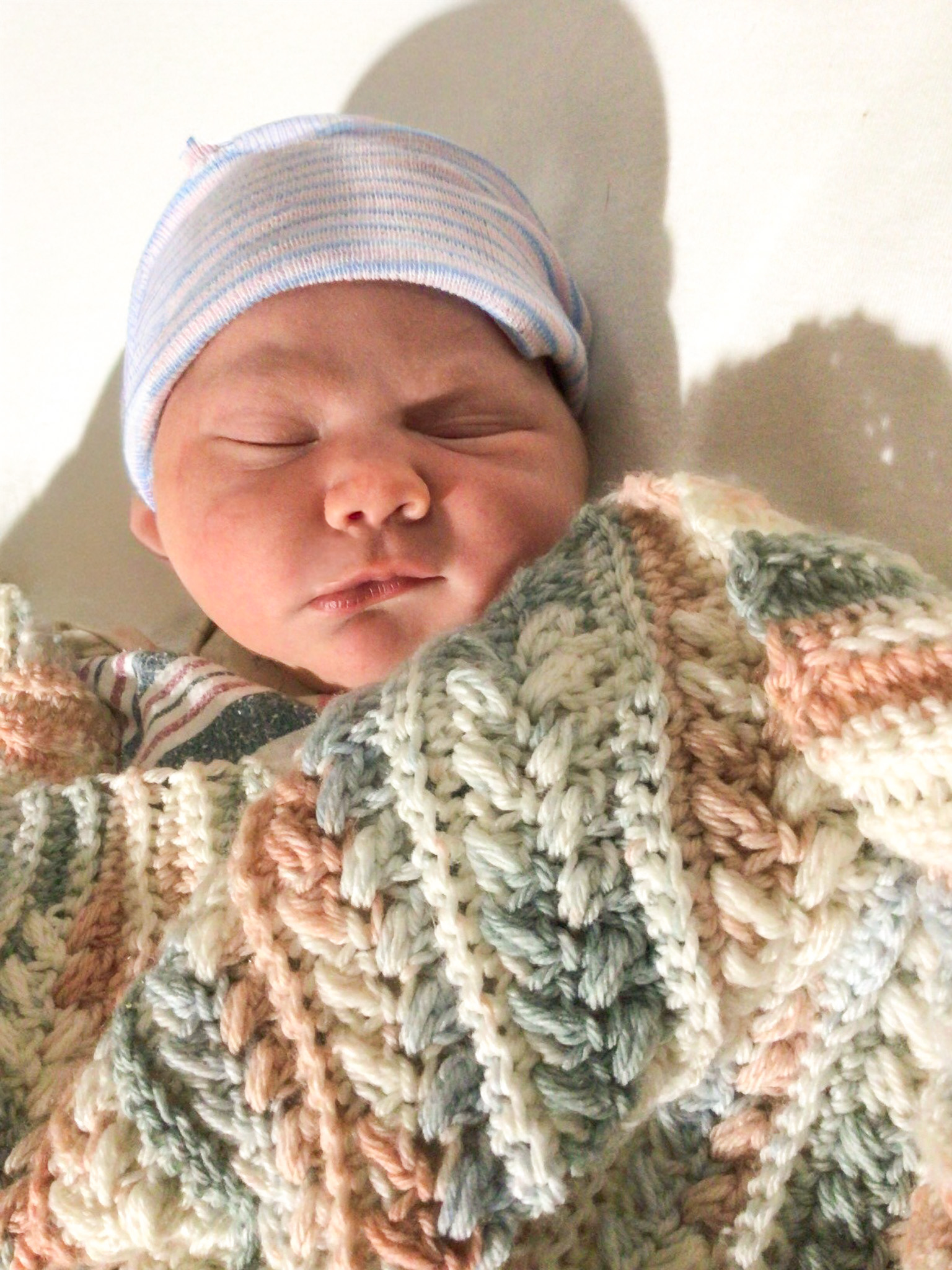 Newborn baby sleeping peacefully wrapped in a cozy knitted blanket with a striped hat.