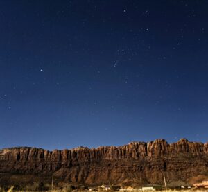 Starry night sky over a rugged mountain ridge with a few lights below, showcasing natural beauty and tranquility.