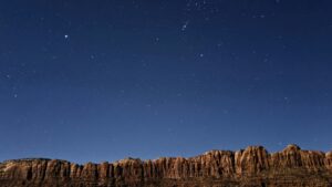 Starry night sky over a rugged mountain ridge with a few lights below, showcasing natural beauty and tranquility.
