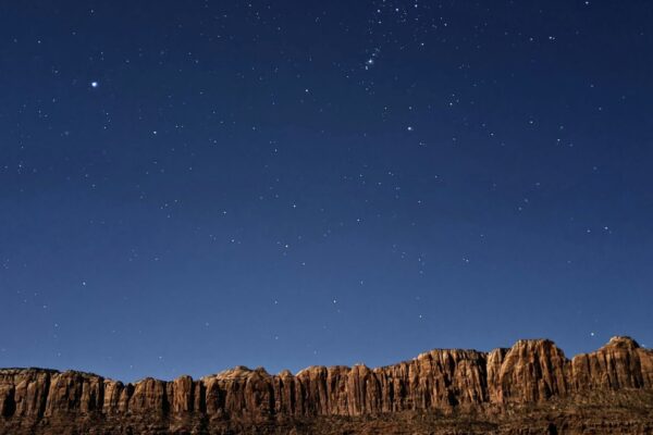 Starry night sky over a rugged mountain ridge with a few lights below, showcasing natural beauty and tranquility.