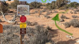 Trailhead sign in desert landscape with text Updraft and Falcon TH. Rocky path surrounded by shrubs under blue sky.