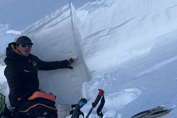 Person assessing snow layers for avalanche safety in a snowy mountain setting.