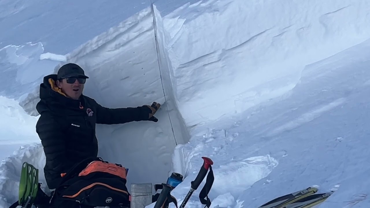Person assessing snow layers for avalanche safety in a snowy mountain setting.