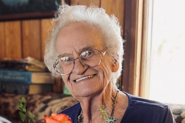 Elderly woman smiling while holding a bouquet of vibrant orange roses indoors.