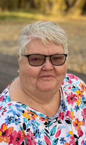 Smiling woman in floral shirt and glasses outside on a sunny day.