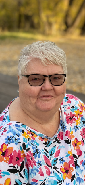 Smiling woman in floral shirt and glasses outside on a sunny day.
