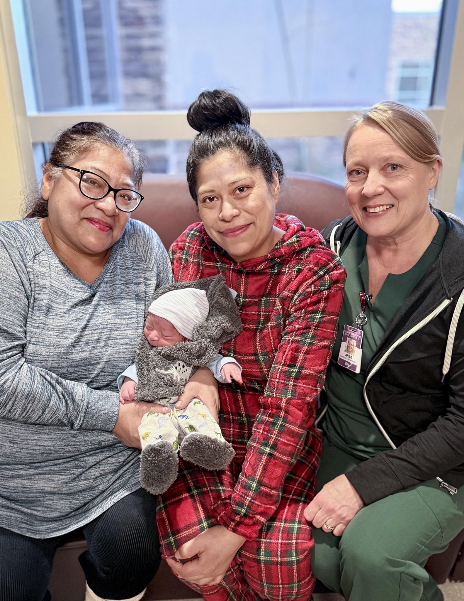 Family and nurse smiling with newborn baby wrapped in cozy outfit inside hospital room.