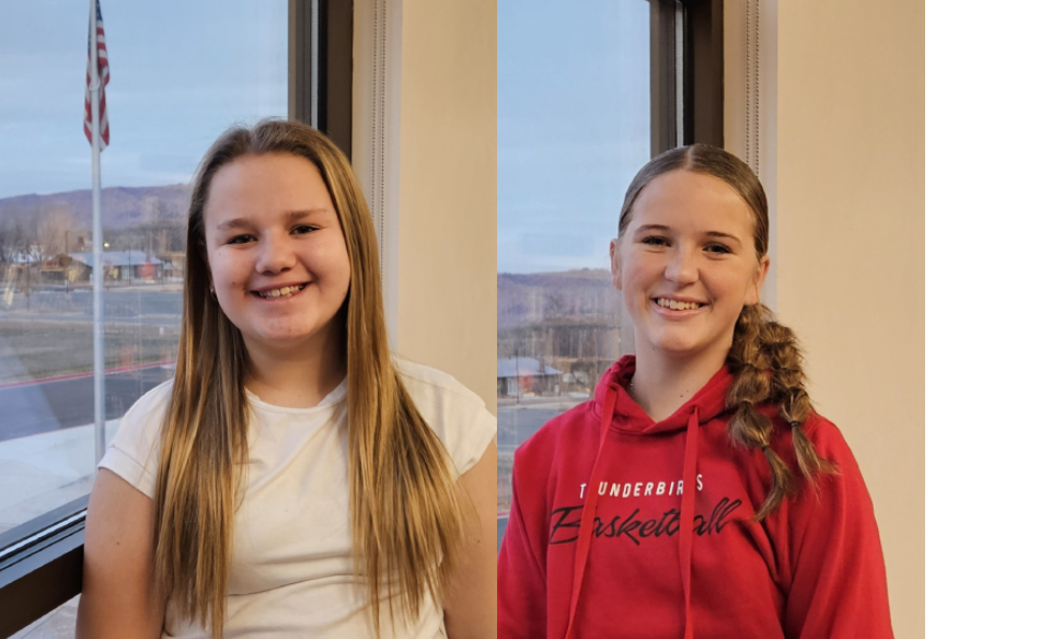Two smiling girls indoors, one in a white shirt and the other in a red hoodie, with an American flag outside the window.