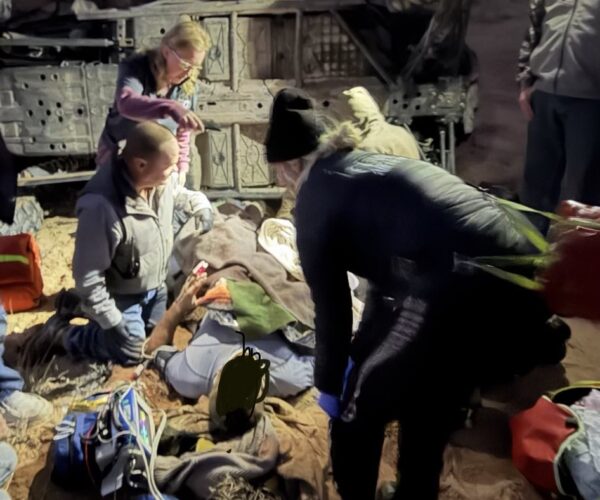 Rescue team aiding an injured person at an off-road rollover scene in a canyon setting.