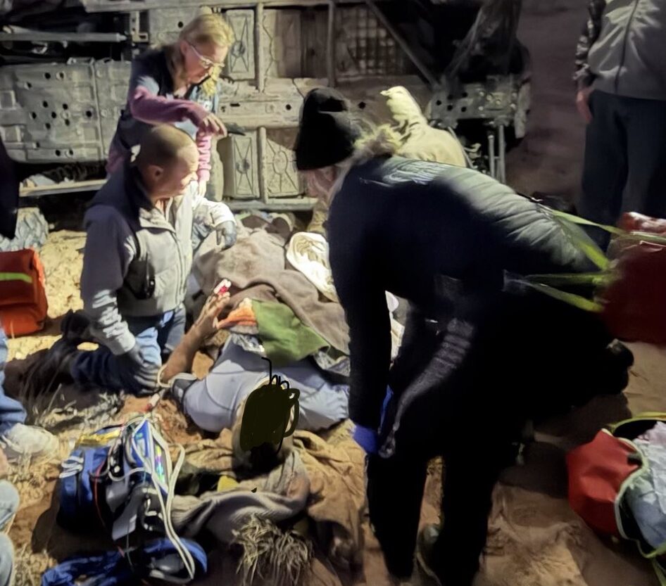 Rescue team aiding an injured person at an off-road rollover scene in a canyon setting.